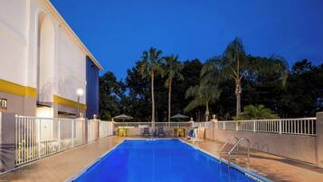 Una piscina con valla blanca, palmeras y un edificio con una franja amarilla.