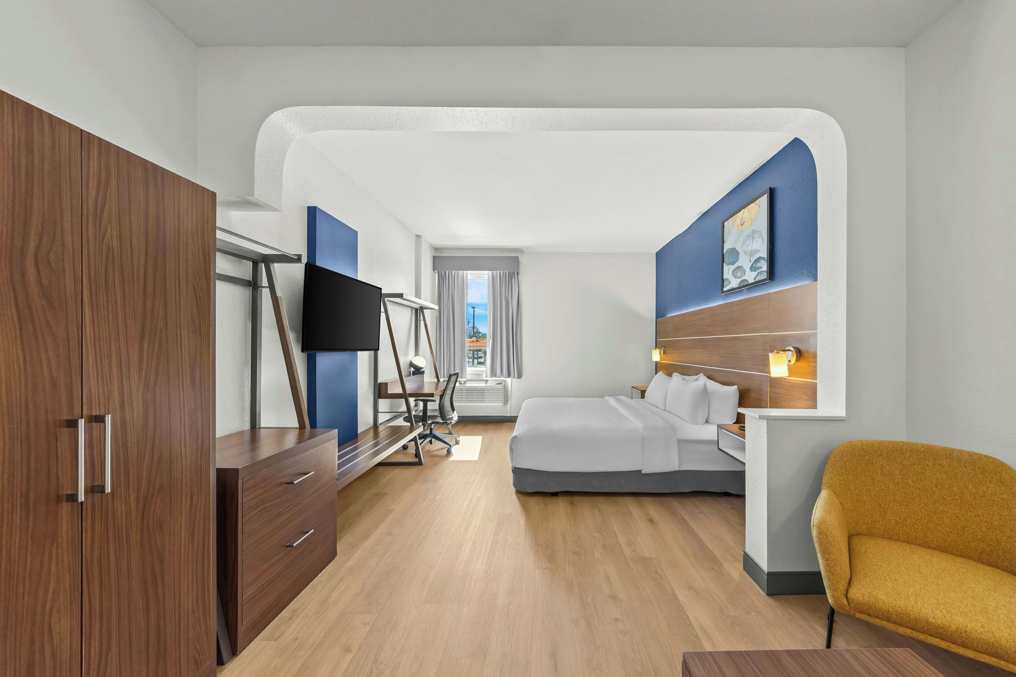 Una habitación de hotel con cama, escritorio, televisor, armario y silla.