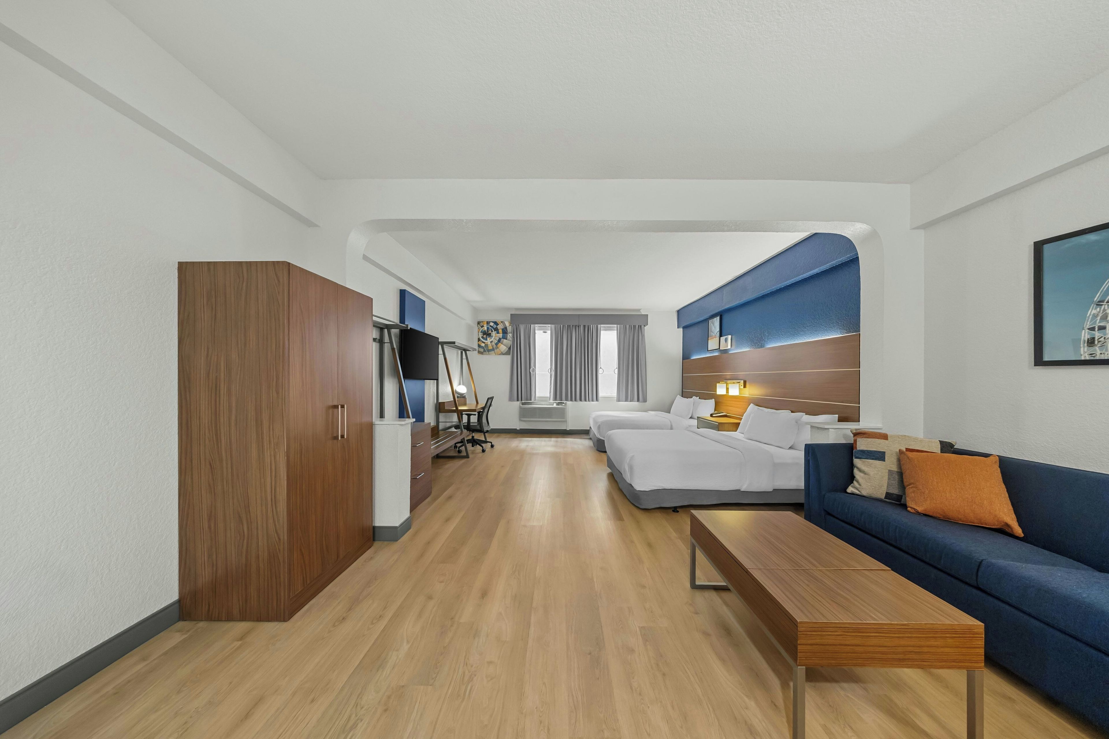 A hotel room with a wooden wardrobe, a sofa, a desk, and a bed.