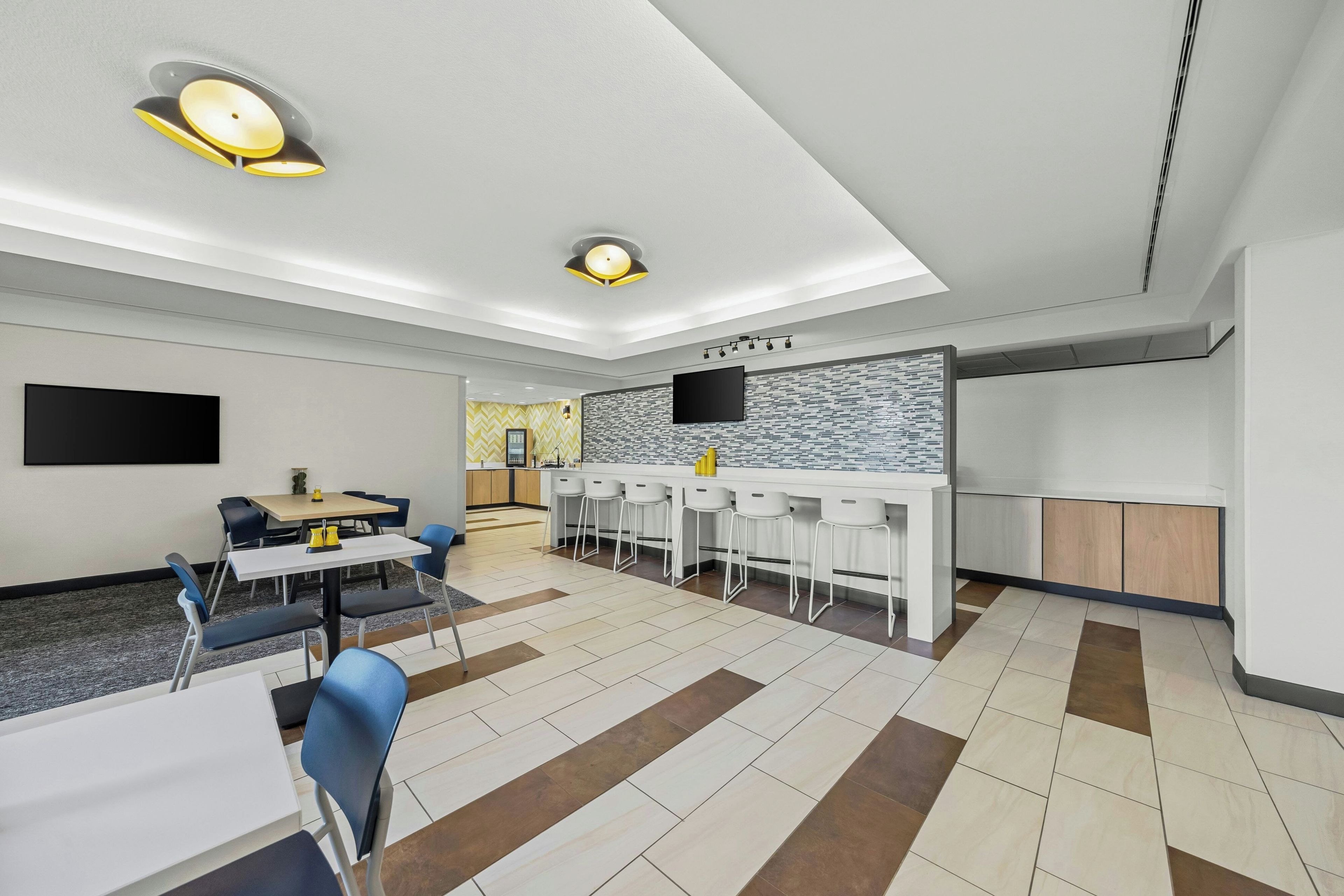 Una habitación de hotel moderna con comedor, cocina y televisor montado en la pared.
