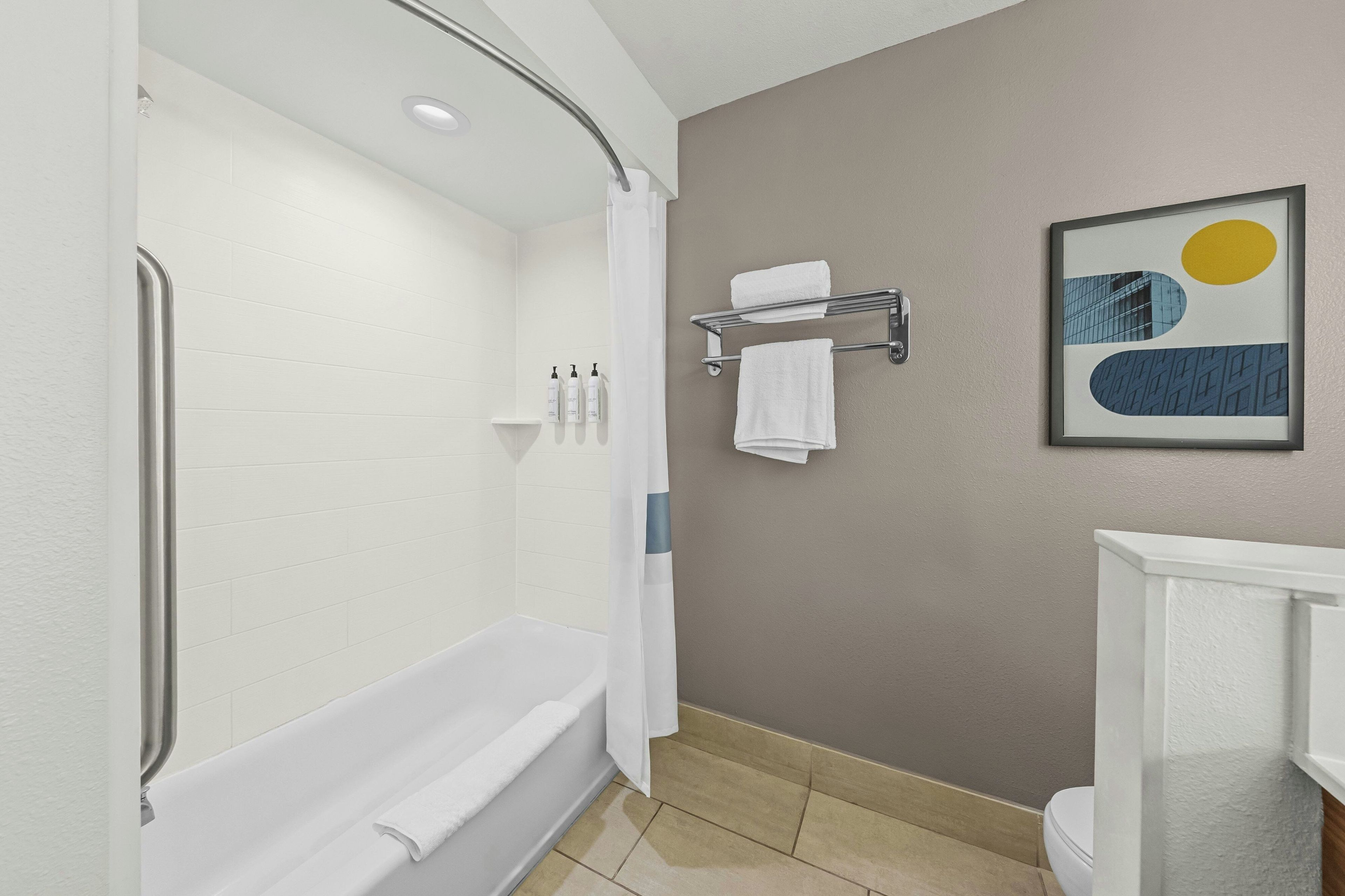 Un baño moderno con cabina de ducha, bañera y un inodoro. Hay dos toallas blancas en un perchero y un cuadro en la pared.