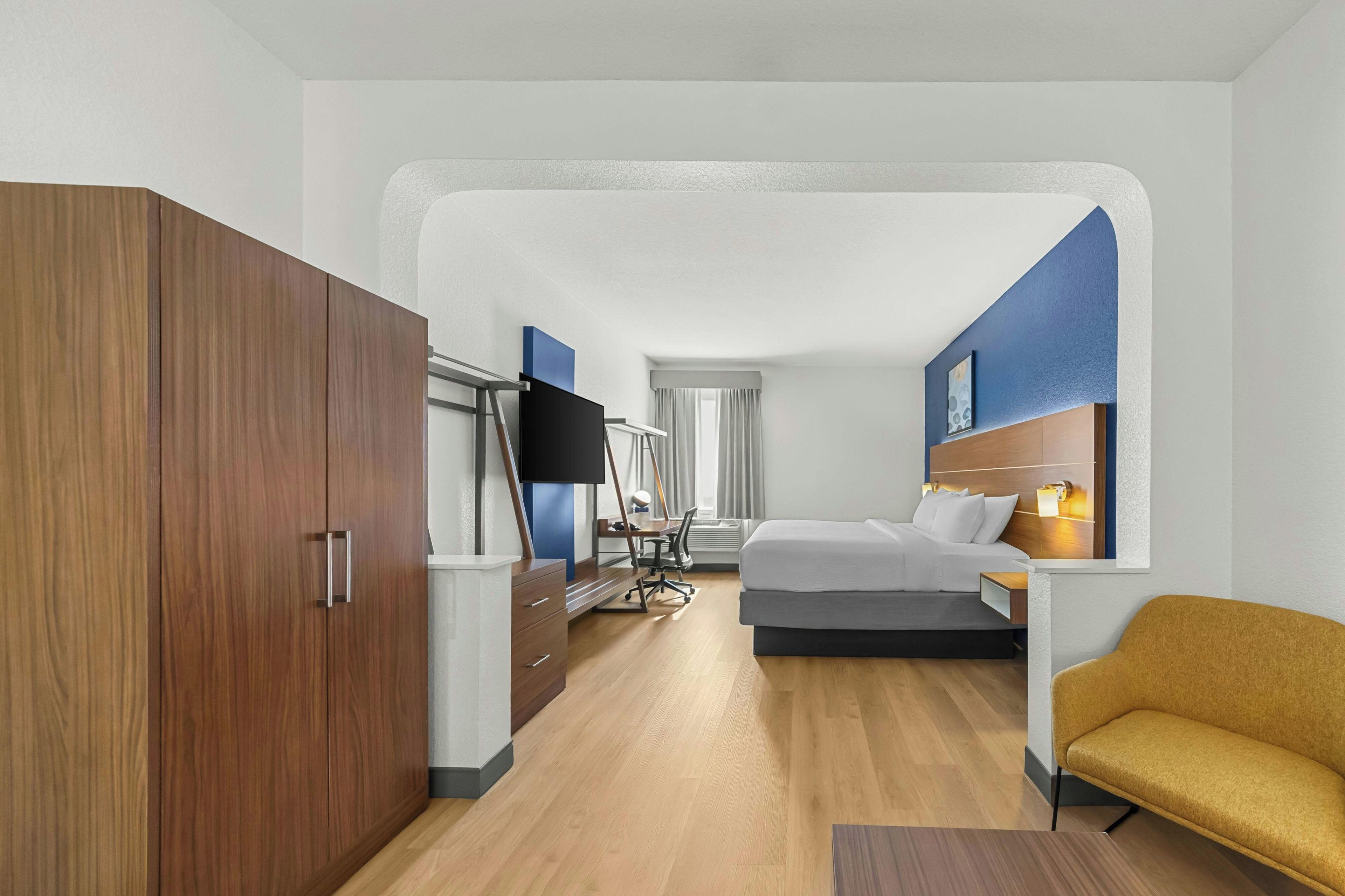 Una habitación de hotel con cama, escritorio, silla y armario.
