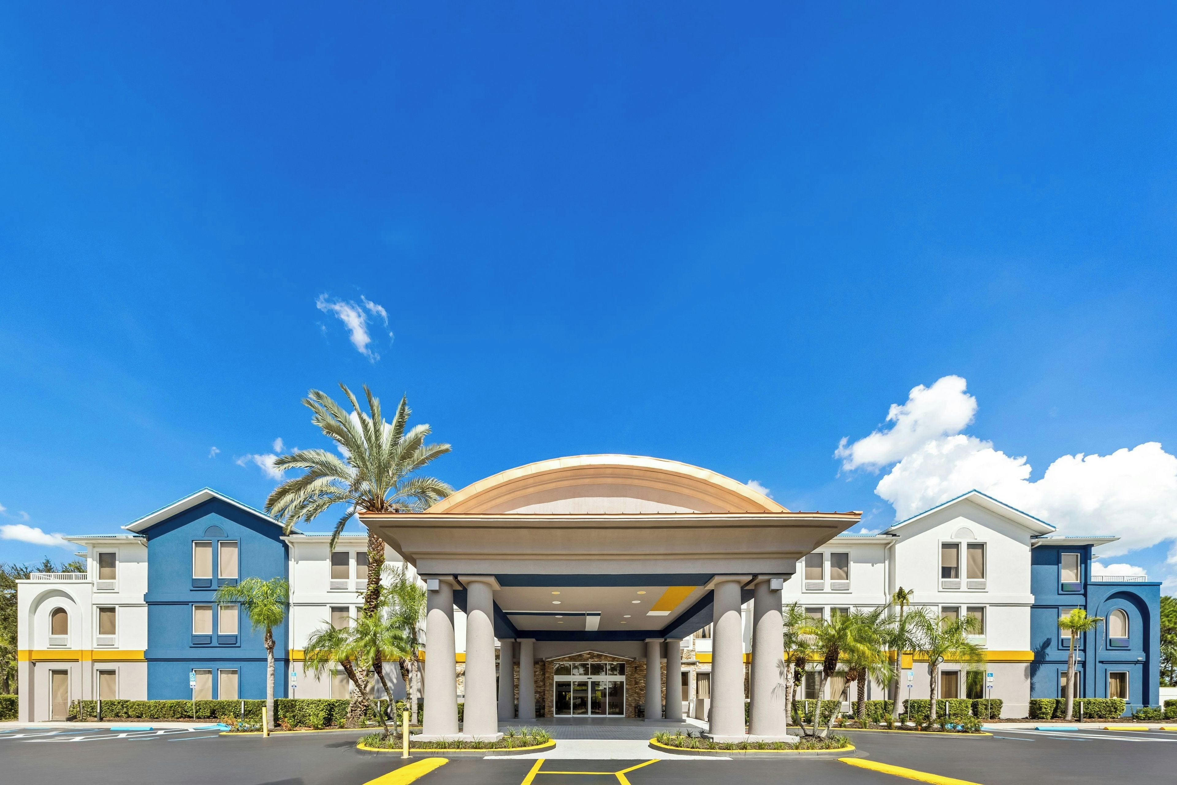 Entrada de un hotel con un corredor cubierto, palmeras y un cielo azul despejado.