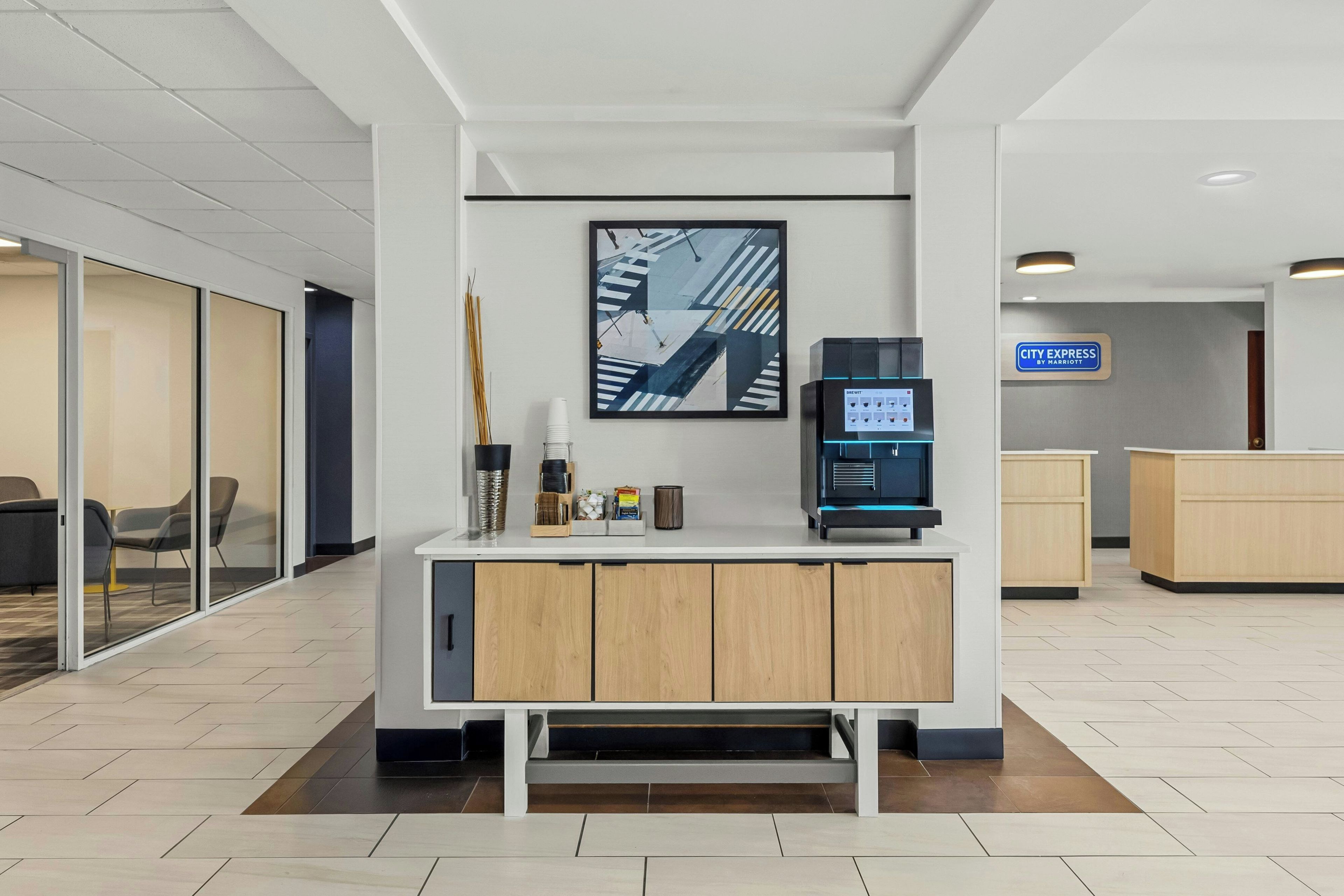 A reception desk with a coffee machine, a framed cityscape artwork, and a sign for City Express by Marriott.