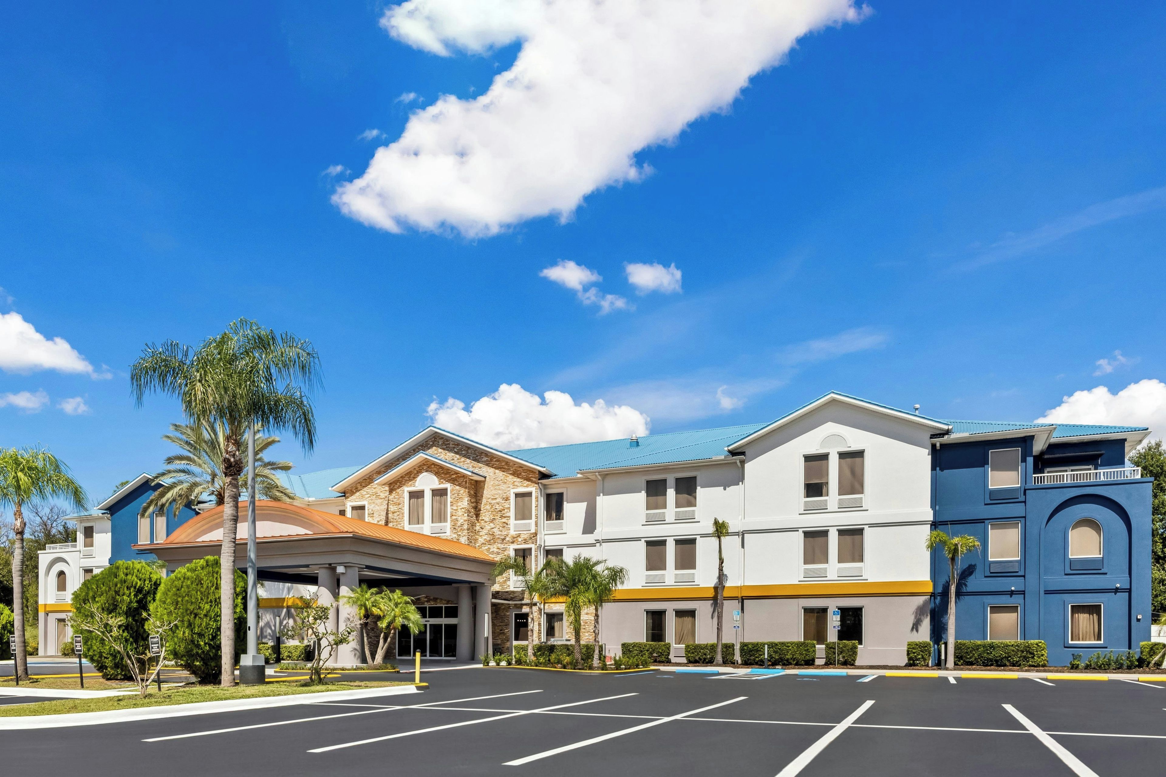 Un hotel con estacionamiento, varias edificaciones y palmeras.