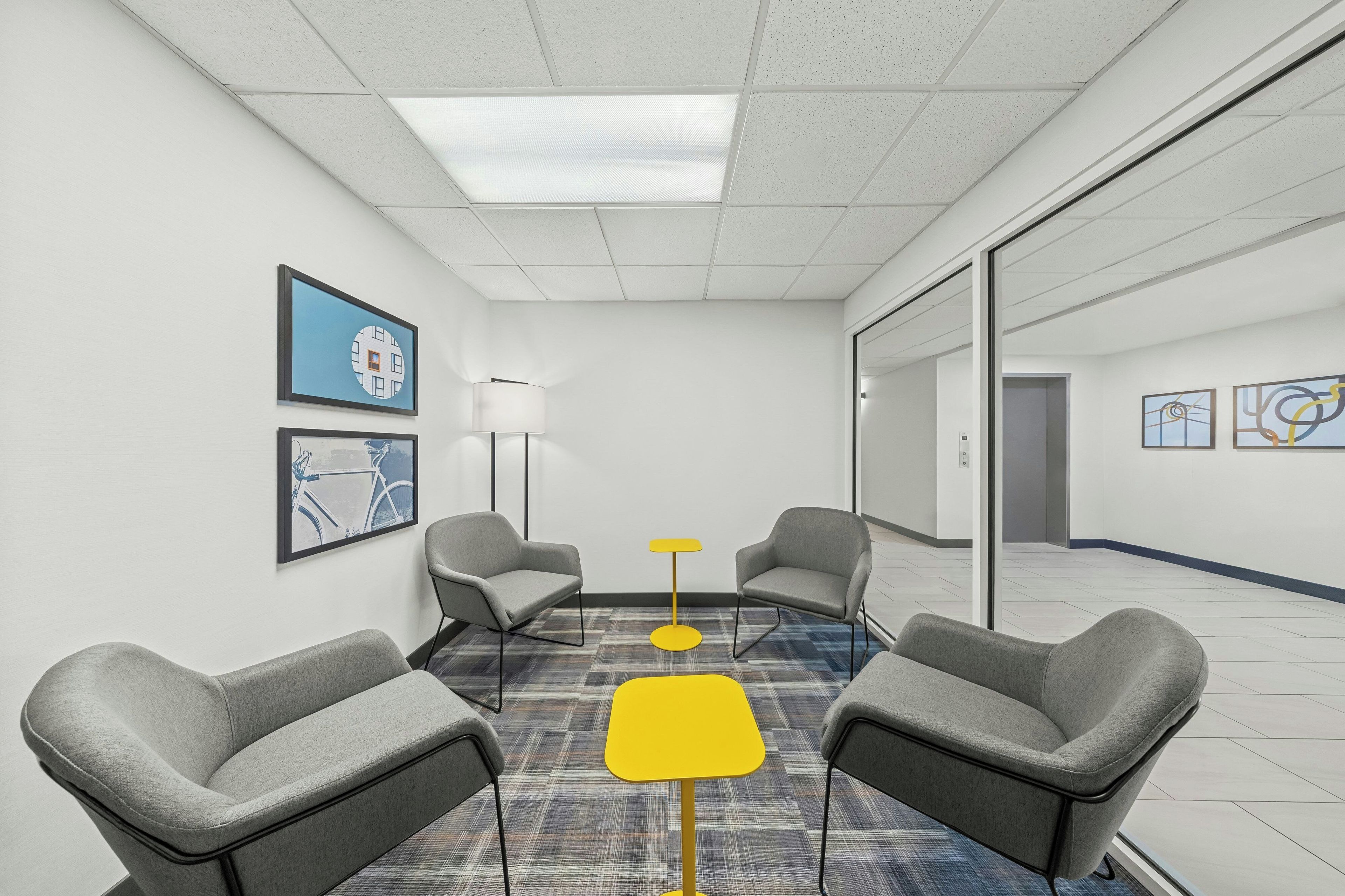 Une salle de conférence dotée d’un sol recouvert de moquette, de deux fauteuils, d’un lampadaire et d’œuvres d’art encadrées accrochées aux murs.