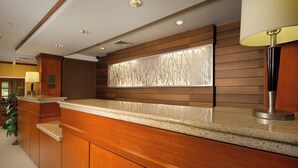 Un espace d’accueil d’hôtel avec un comptoir de réception en bois, un grand mur décoratif et une plante en pot.