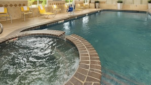 Une piscine avec un jacuzzi, des chaises longues et un panneau indiquant la présence d’un sauveteur.