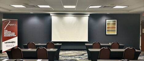 Un salón de conferencias con una pantalla de proyector, mesas y sillas.