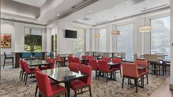 A conference room with multiple tables and chairs, large windows, and a flat-screen TV.