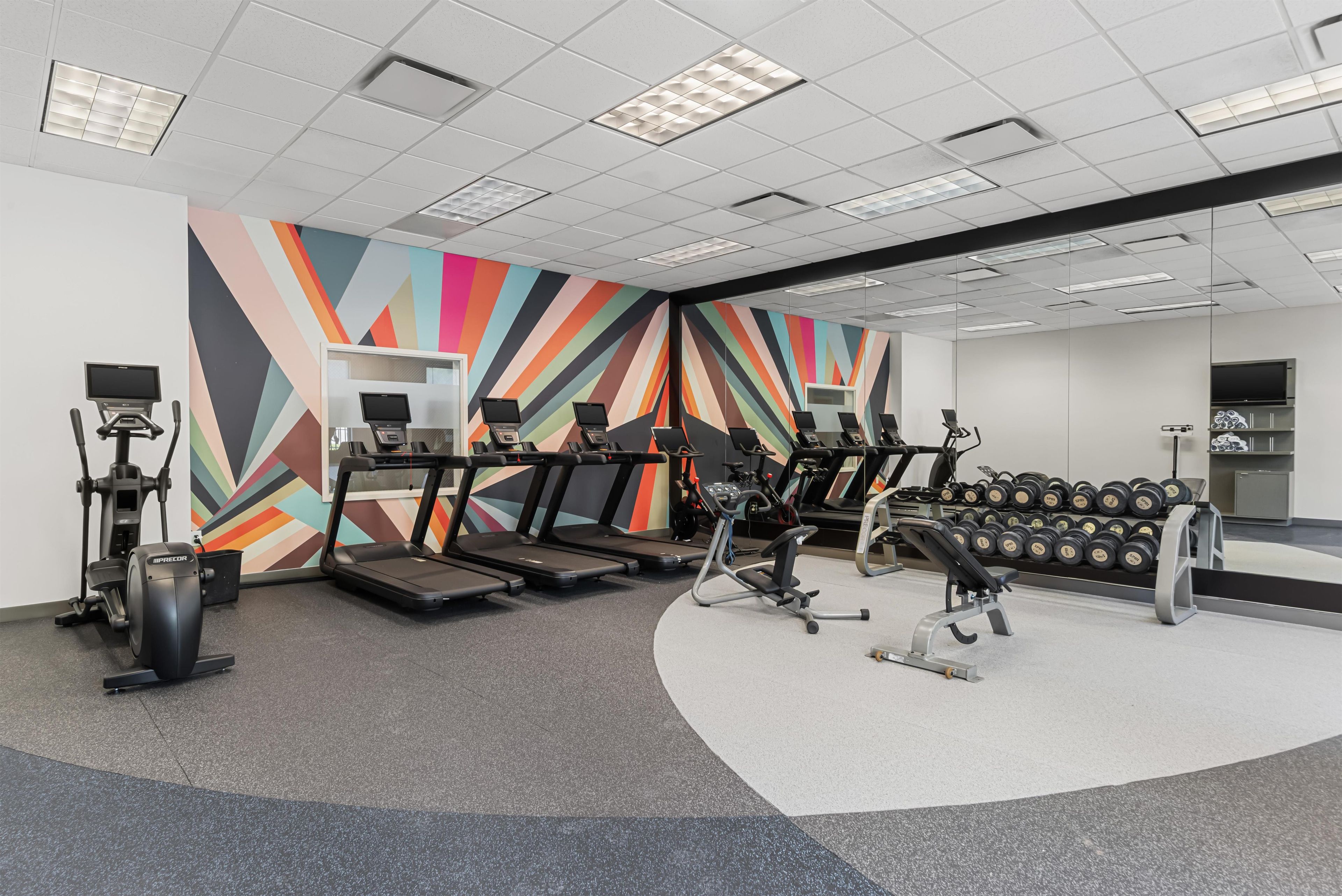 A gym with treadmills, elliptical machines, and a wall with a geometric pattern.