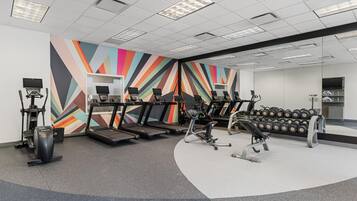 A gym with treadmills, elliptical machines, and a wall with a geometric pattern.