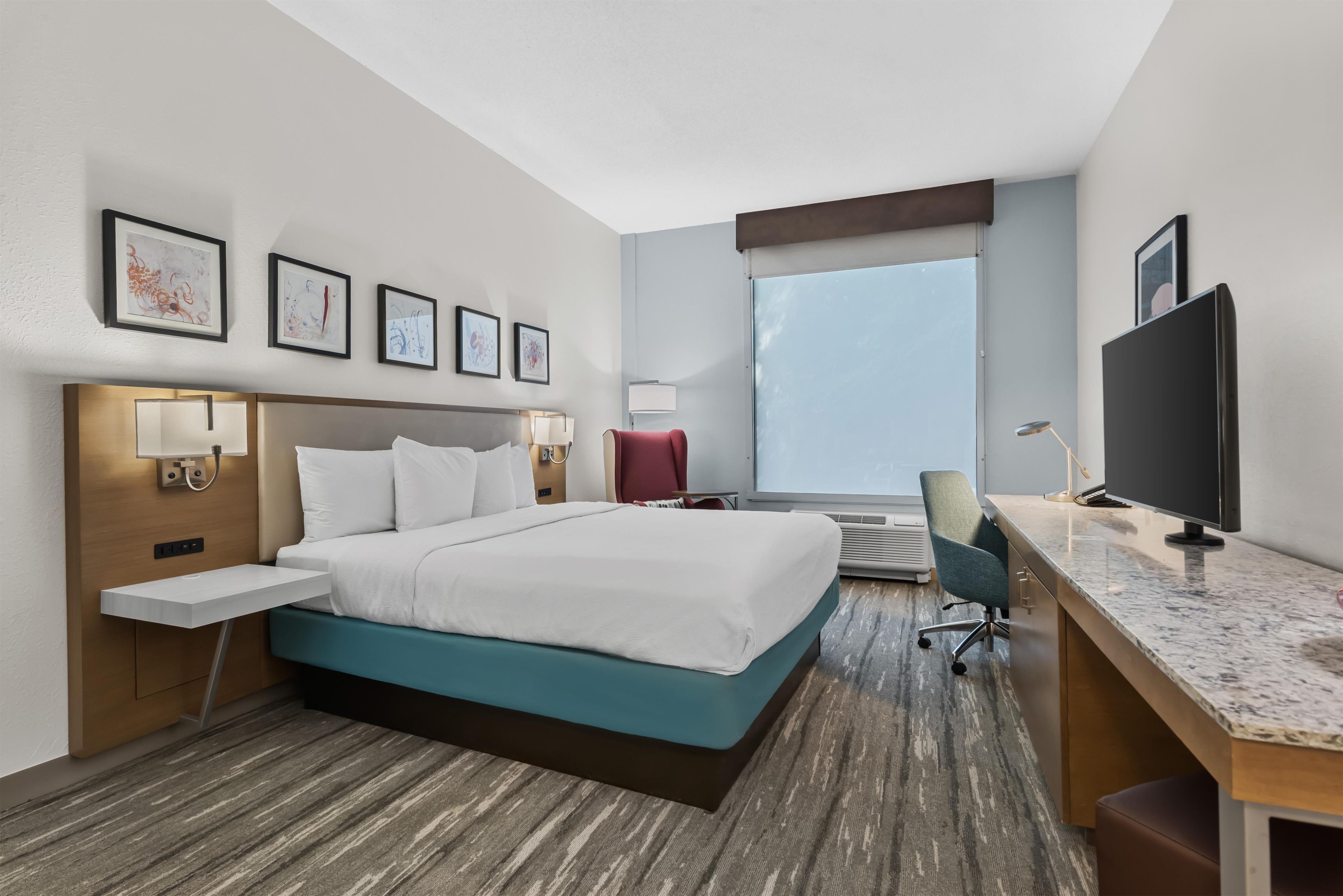 Habitación de hotel con cama, escritorio, televisor y una obra de arte en la pared.