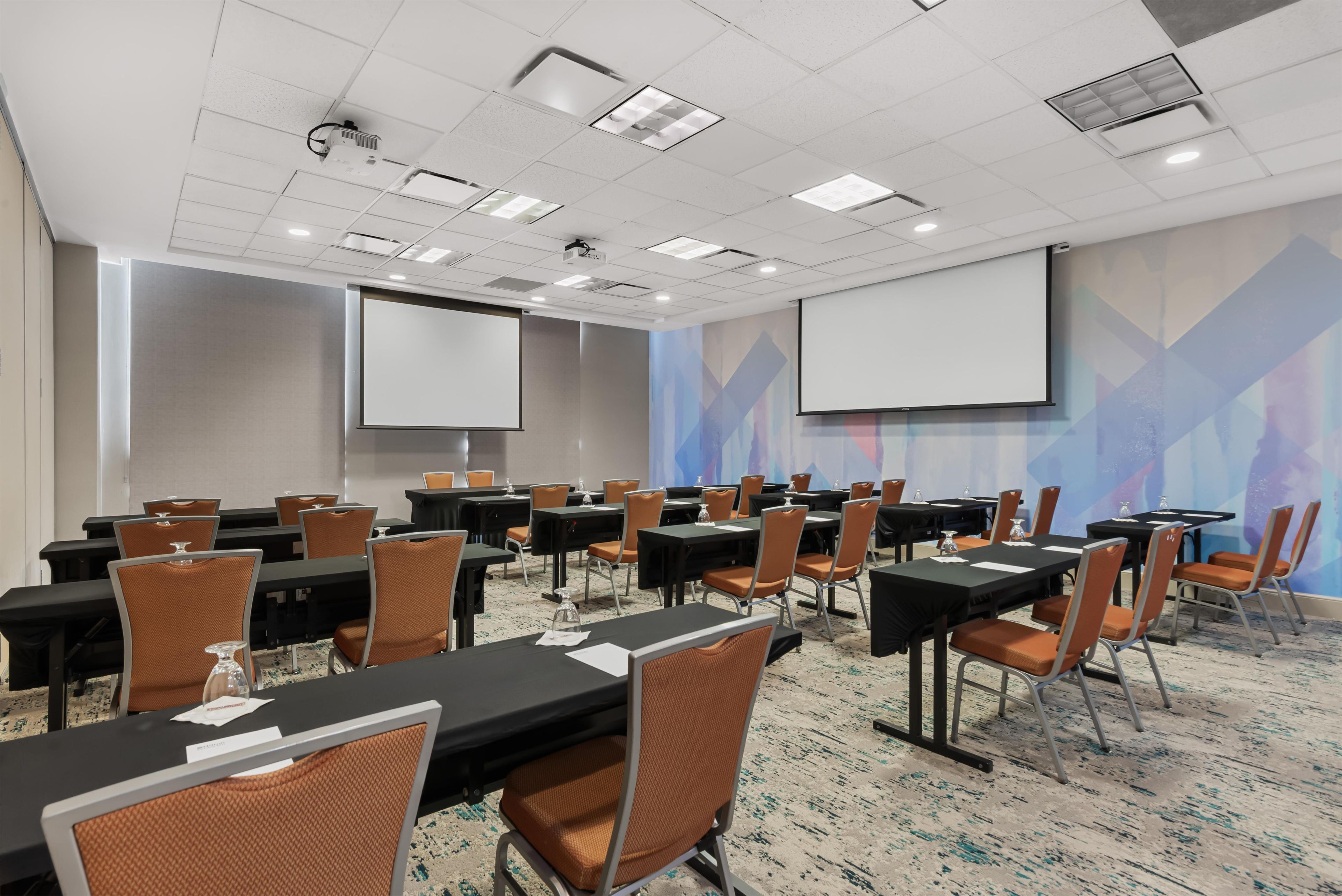 A conference room with multiple tables and chairs, equipped with projectors and screens.