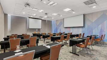 A conference room with multiple tables and chairs, equipped with projectors and screens.
