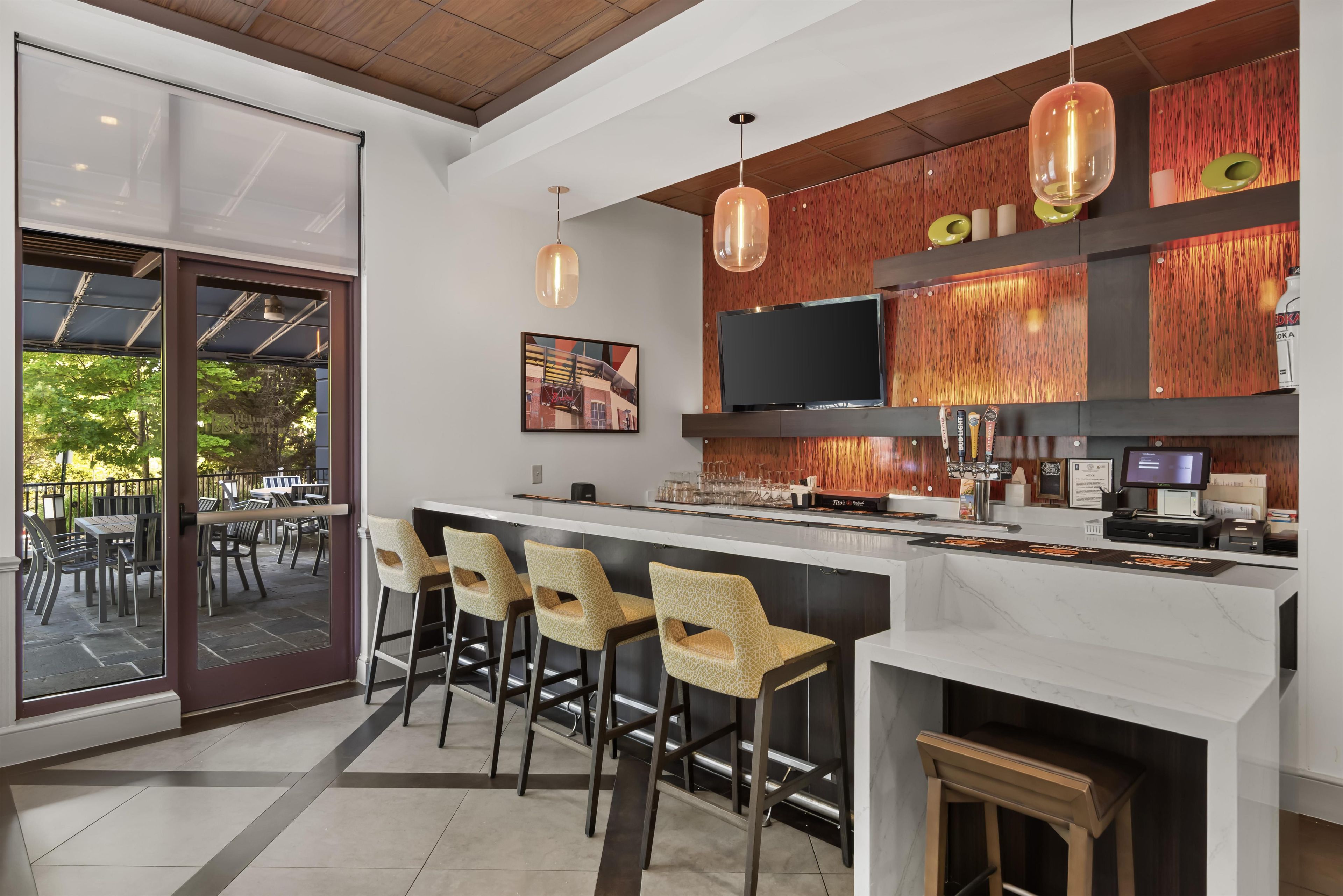 Een moderne bar met een wit aanrecht, barstoelen en een televisie boven de bar.