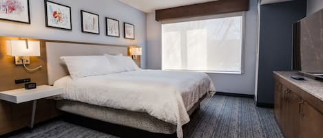 A hotel room with a bed, bedside tables with lamps, a TV, and artwork on the wall.