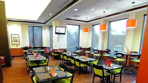 A restaurant with multiple tables and chairs, large windows, and a television on the wall. - Hilton Garden Inn Atlanta Marietta (Atlanta)