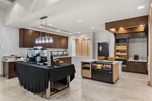 Une cuisine moderne avec un coin repas, équipée de machines à café, d’un réfrigérateur et d’un distributeur de boissons.
