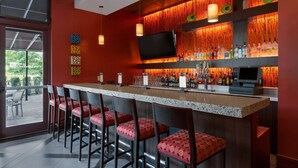 A bar area with a long counter, multiple bar stools, a flat-screen TV, and a wall of hanging bottles. - Hilton Garden Inn Atlanta Marietta (Atlanta)