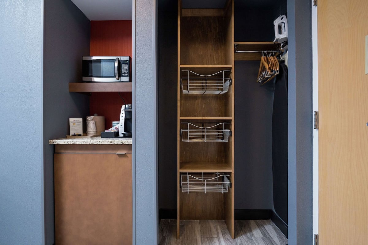 Cocina compacta con microondas, cafetera y estantes para guardar objetos.