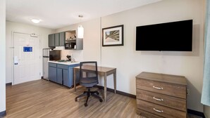 Una habitación compacta con kitchenette, escritorio, silla, televisor y cómoda.