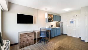 Un apartamento moderno con kitchenette, un televisor de pantalla plana montado en la pared, un escritorio de madera con una silla y un pequeño calentador.