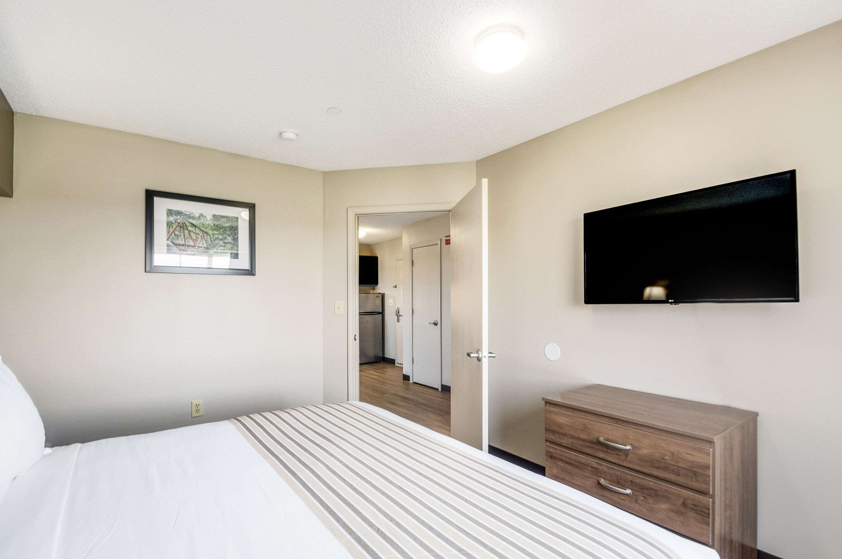 A hotel room with a bed, a dresser, a flat-screen TV mounted on the wall, and a framed picture on the wall.
