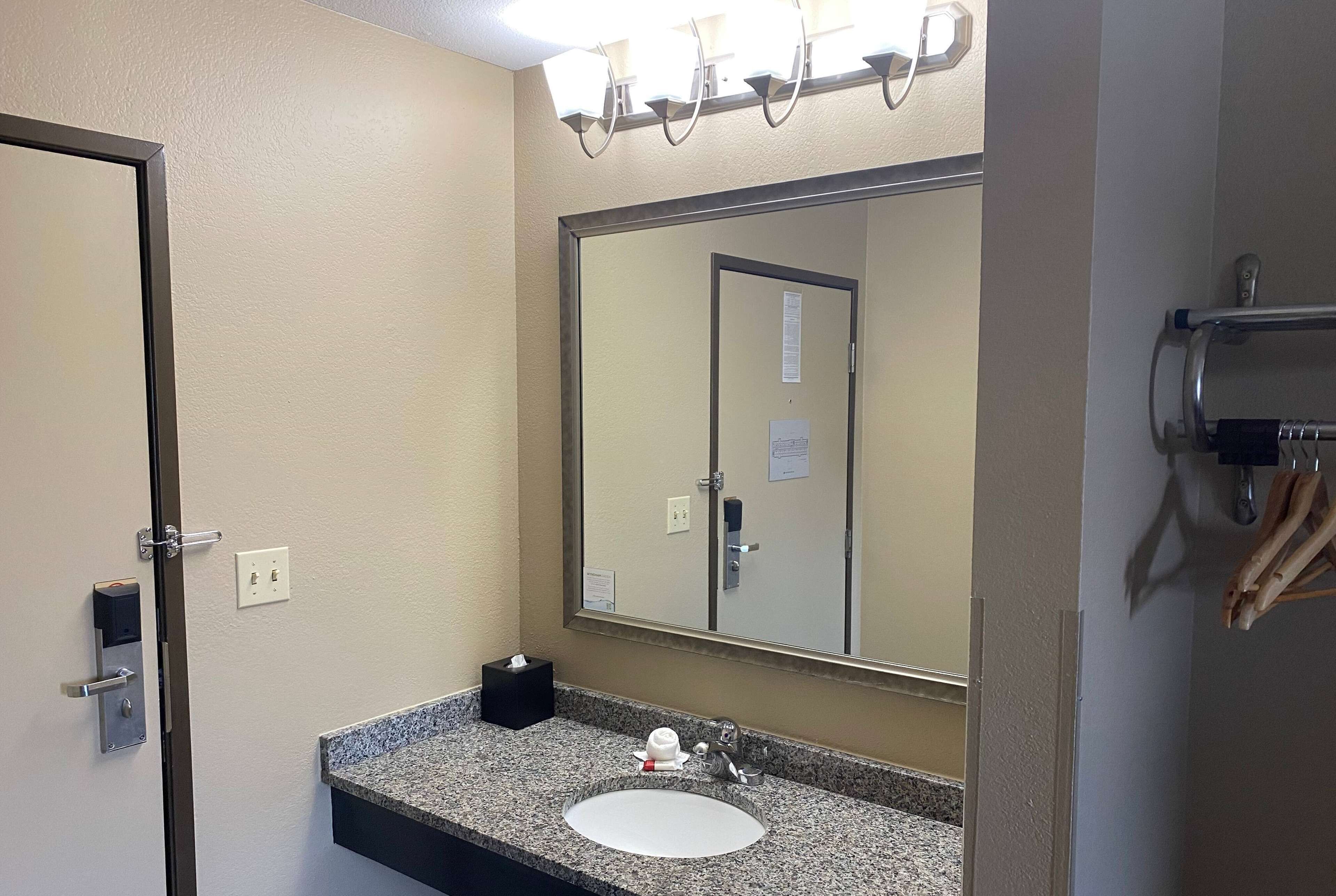 A hotel bathroom with a sink, mirror, towel rack, and a door.