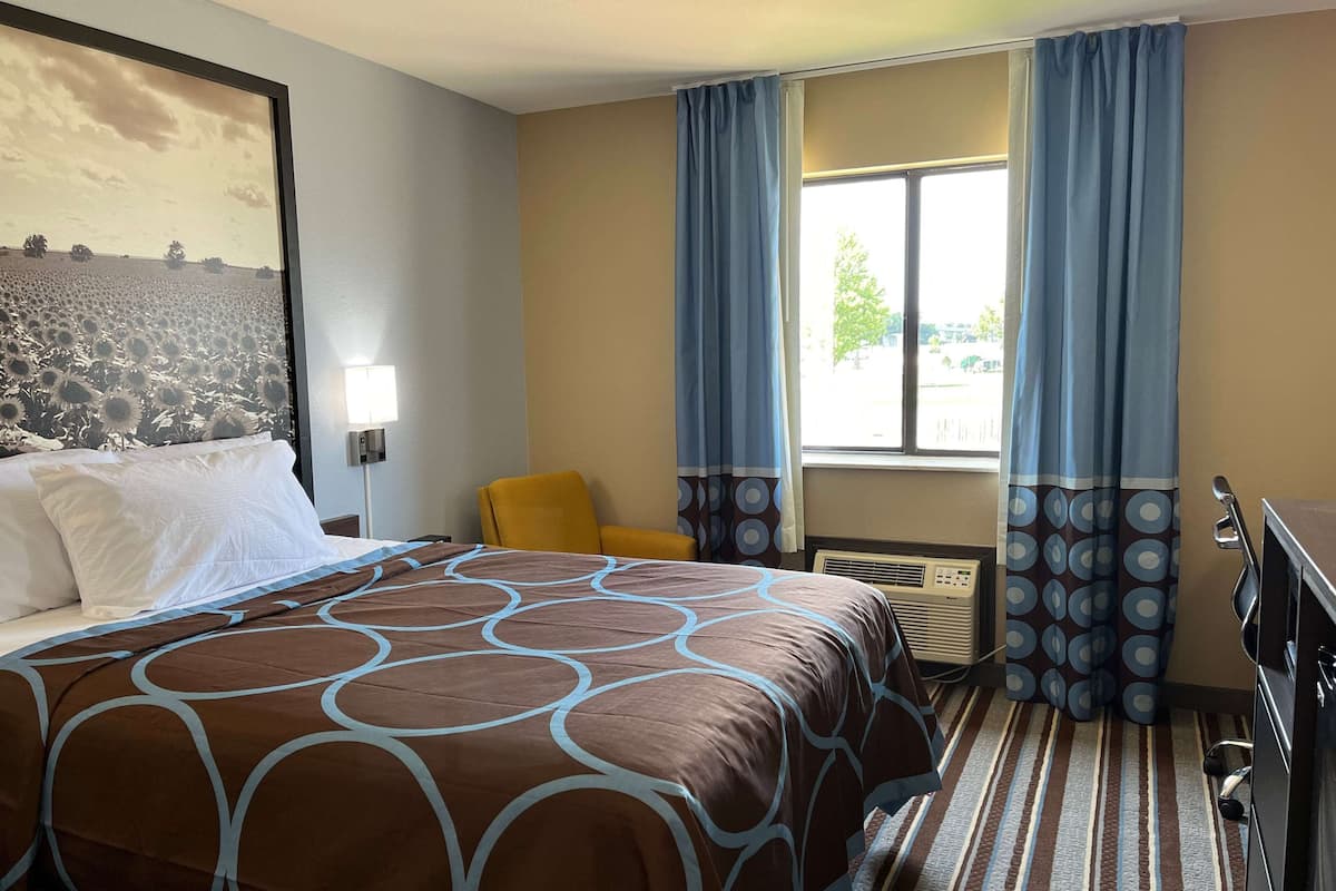 A hotel room with a large bed, a chair, a desk, and a window with curtains.