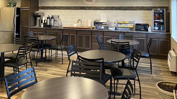 A modern kitchen with built-in appliances, a breakfast sign, and a dining area with tables and chairs. - Super 8 by Wyndham Independence KS (Independence)