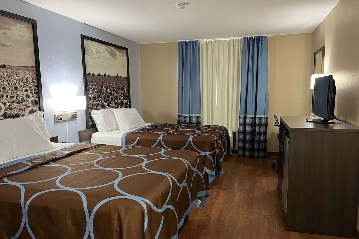 A hotel room with two beds, a desk, a television, and a window with curtains.