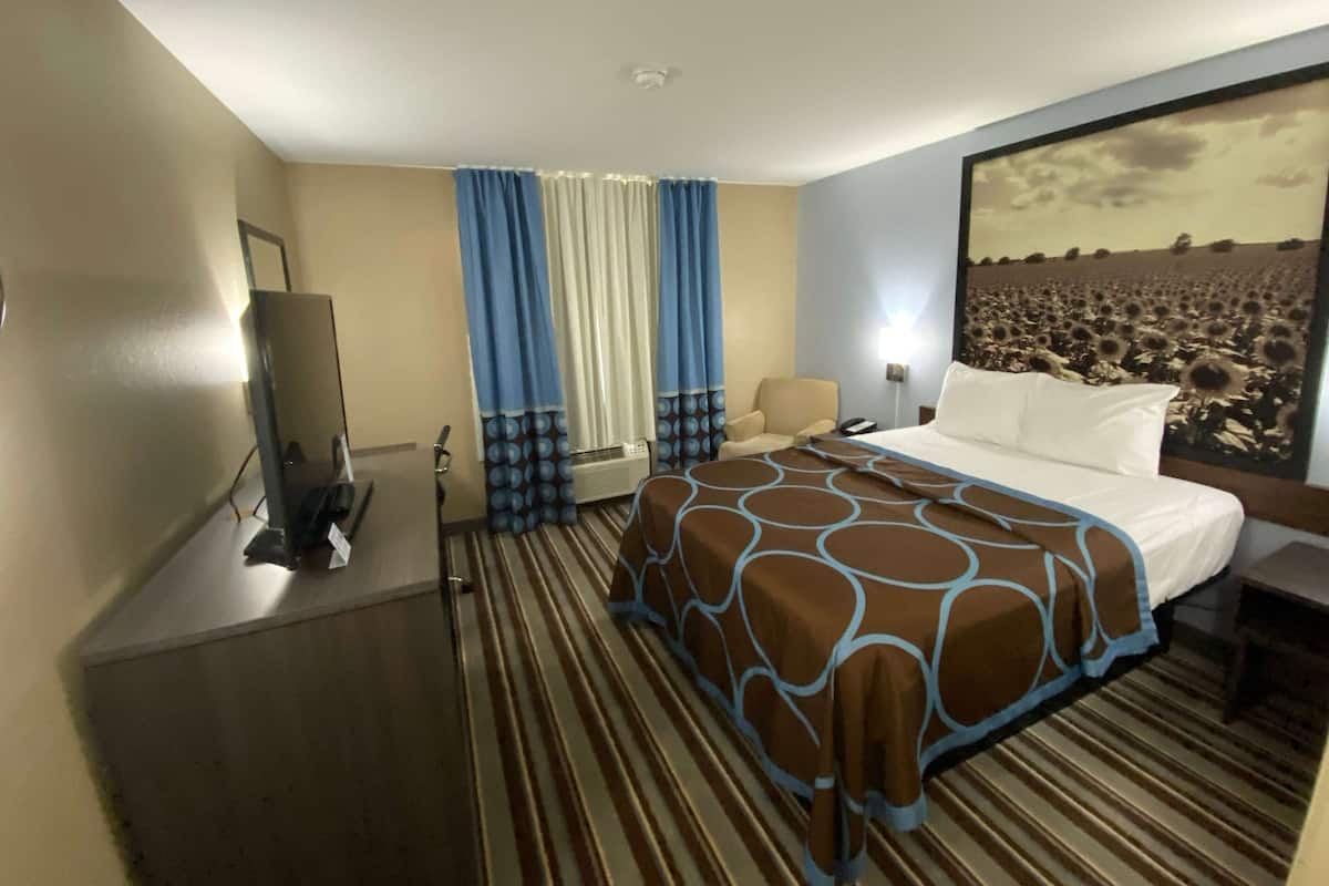 A hotel room with a bed, a desk, a TV, and a large window with curtains.