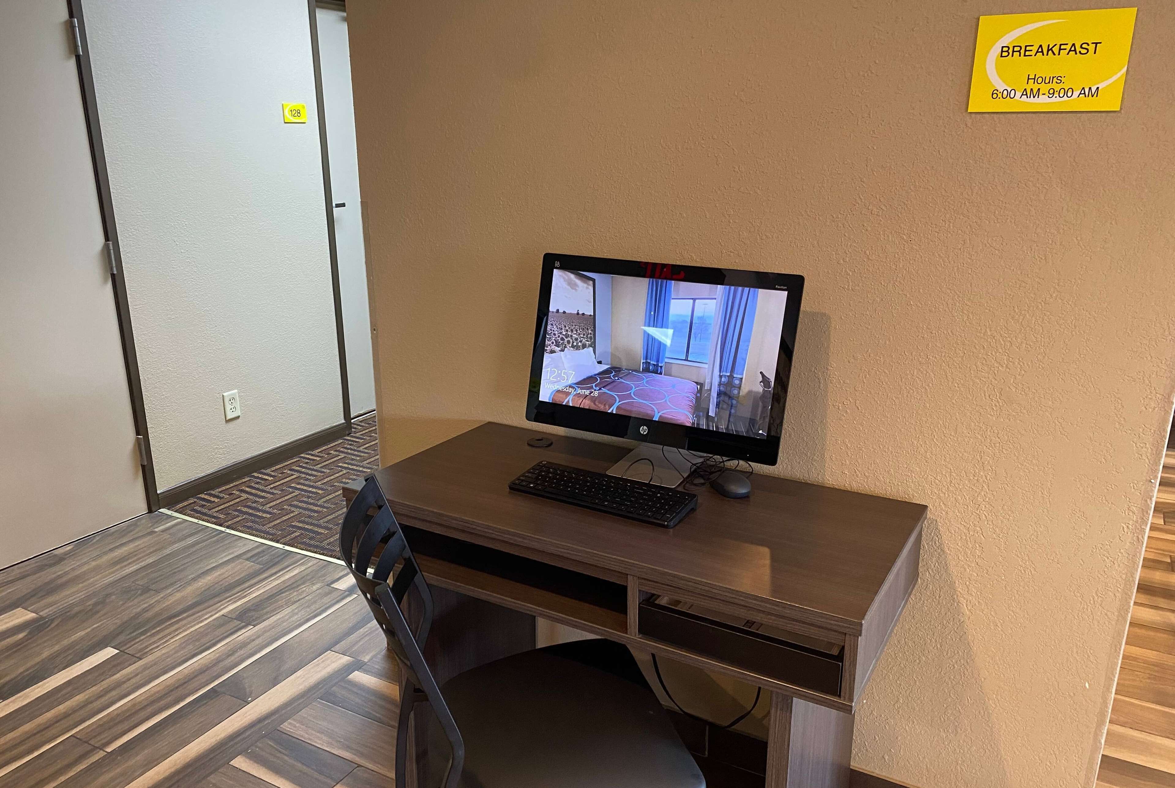 A hotel room with a computer desk, a chair, and a bed. There is a sign indicating breakfast hours.