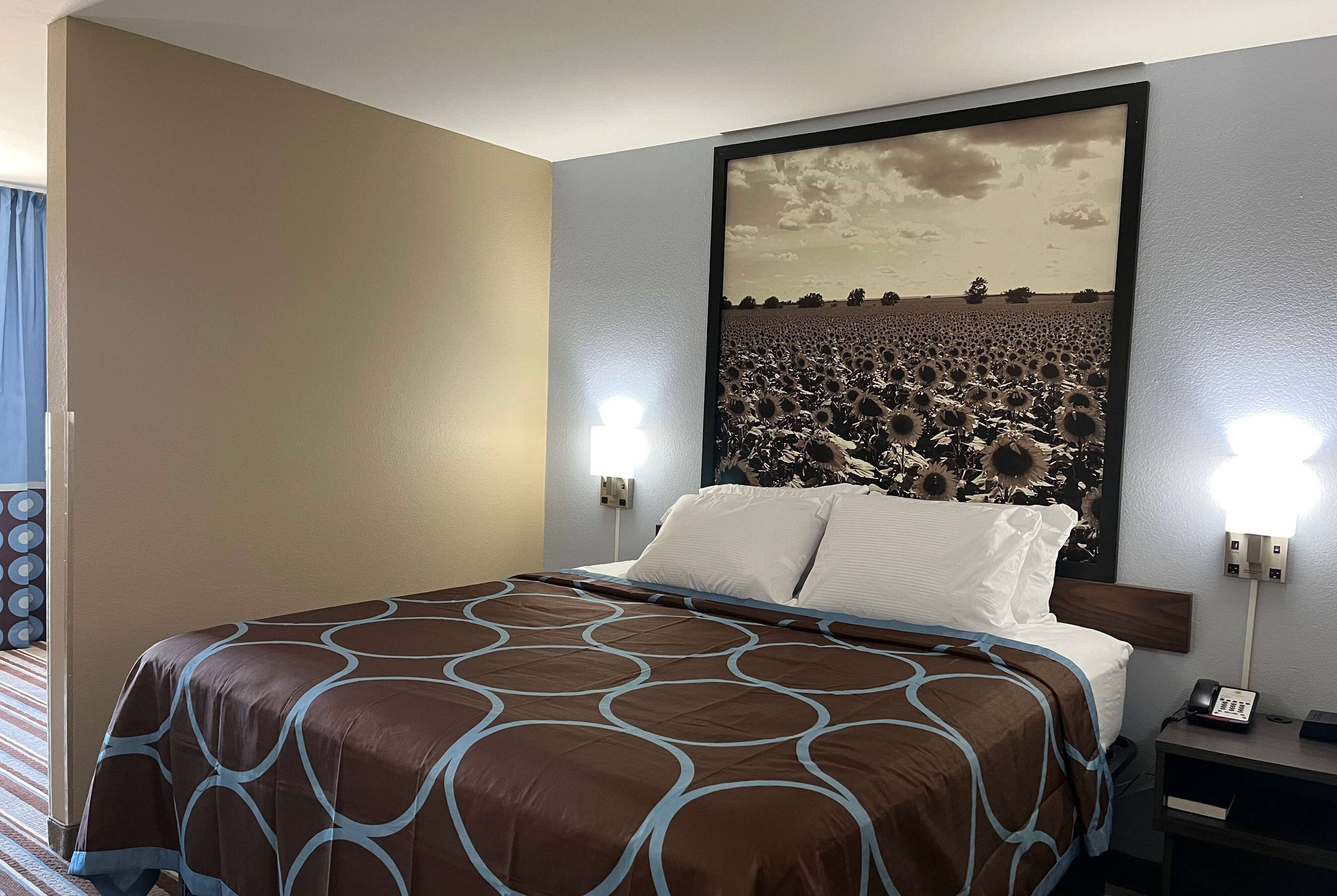 A hotel room with a large bed, a headboard with a sunflower mural, bedside lamps, and a nightstand with a phone.