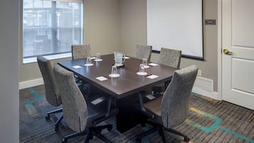 A conference room with a large table, six chairs, a projector screen, and a storage sign on the wall.