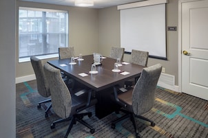 A conference room with a large table, six chairs, a projector screen, and a storage sign on the wall.