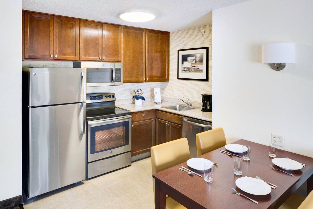 A modern kitchen with stainless steel appliances, wooden cabinets, and a dining area with a table set for four.
