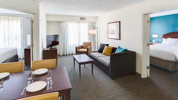 A hotel room with a bed, a sofa, a dining table set with plates and glasses, a TV, and a lamp.