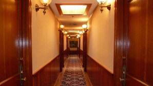 Un pasillo con puertas de madera, apliques en la pared, suelo alfombrado y tragaluz.