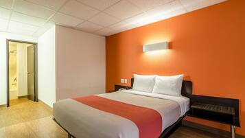 A hotel room with a bed, a nightstand, a wall-mounted light, and a door leading to a bathroom.