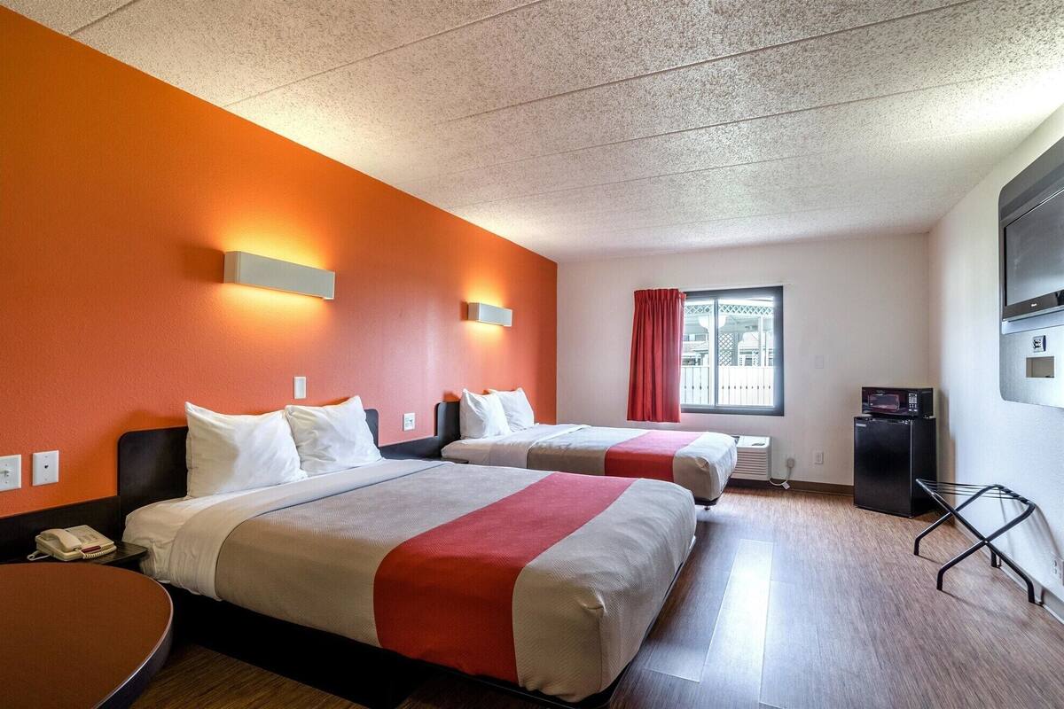 Une chambre d’hôtel avec deux lits, une télévision, un four à micro-ondes et une fenêtre avec des rideaux.