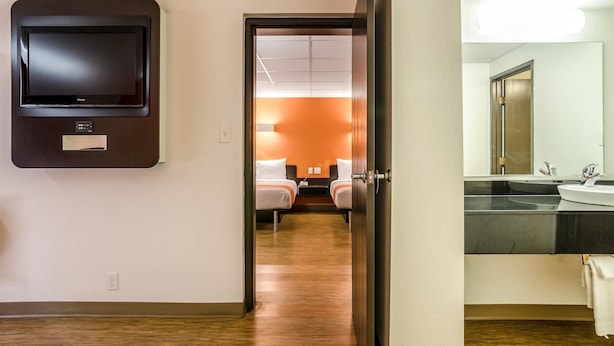 A hotel room with a television, a bed, a small table, and a bathroom with a sink and mirror. - Motel 6 York, NE (York)