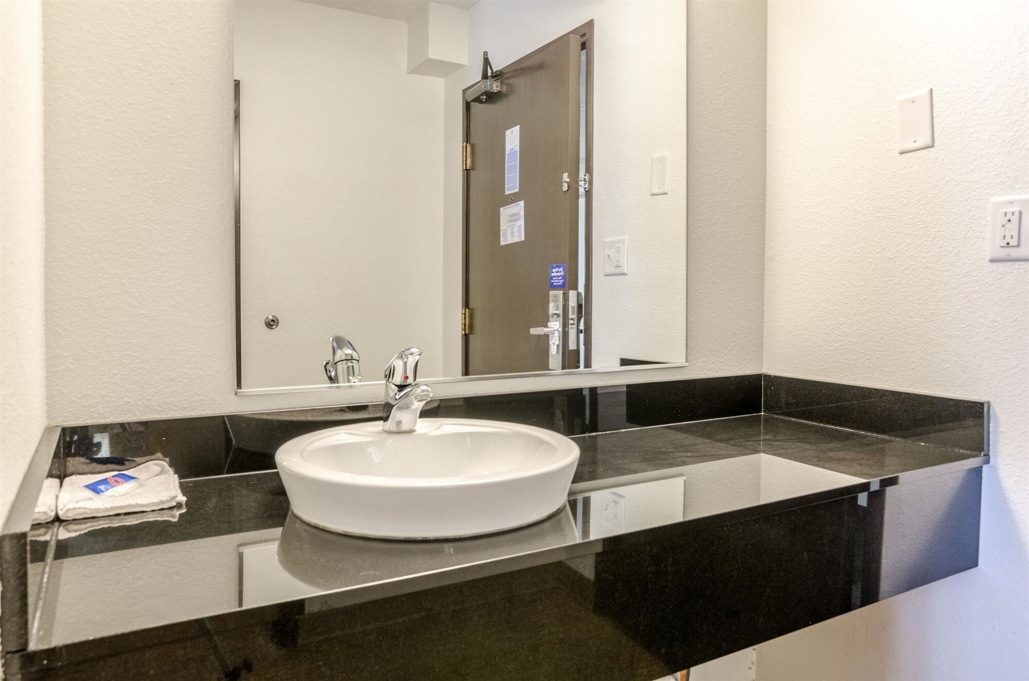 A modern bathroom with a white sink, black countertop, and a large mirror.
