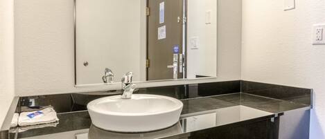 A modern bathroom with a white sink, black countertop, and a large mirror.