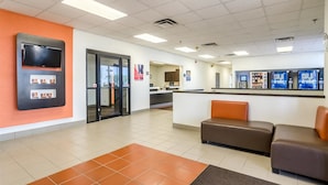 A reception area with a counter, seating, and a TV mounted on the wall. - Motel 6 York, NE (York)