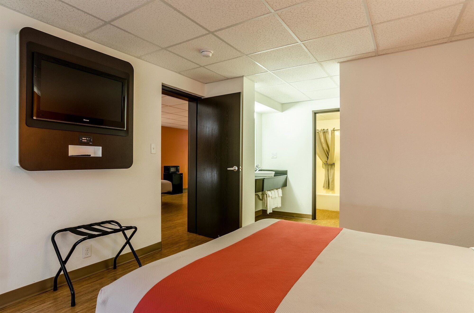 A hotel room with a bed, a TV mounted on the wall, a small table, and a door leading to a bathroom.