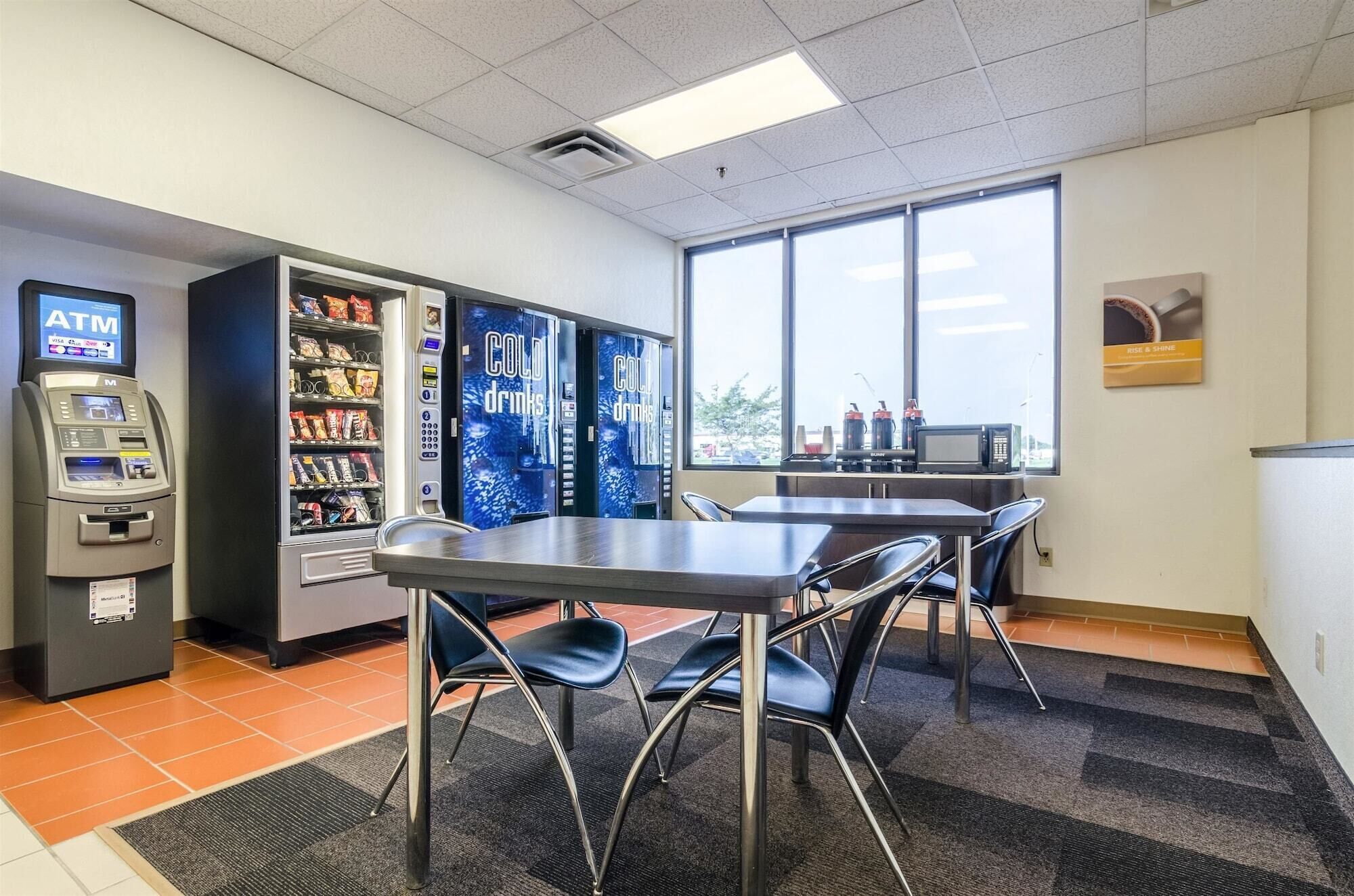 A small indoor space with a vending machine, an ATM, and a table with chairs.