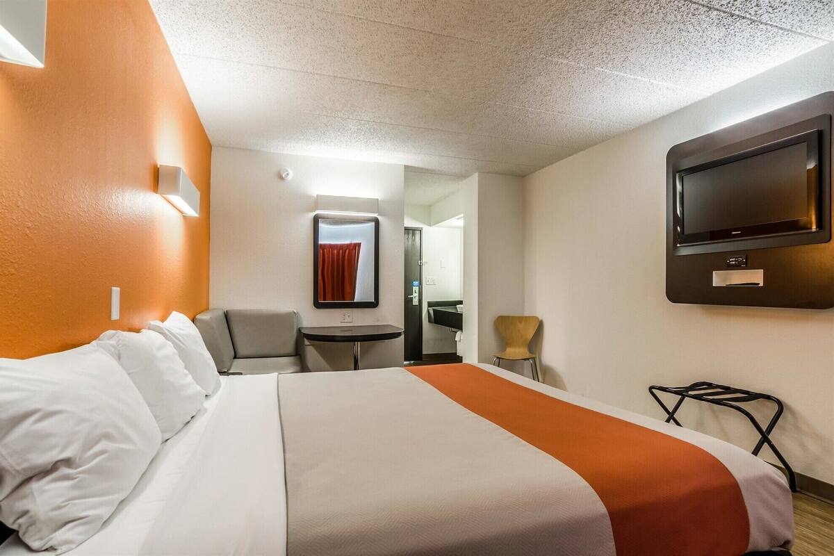 Une chambre d’hôtel avec un lit, un bureau, une chaise, une télévision et une salle de bain visible à travers une porte ouverte.