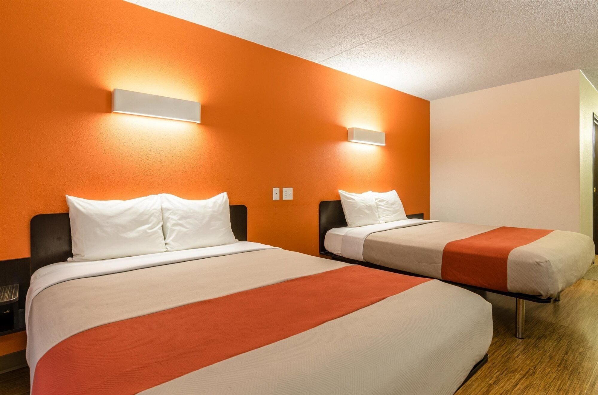 A hotel room with two beds, each with white bedding and orange accents.